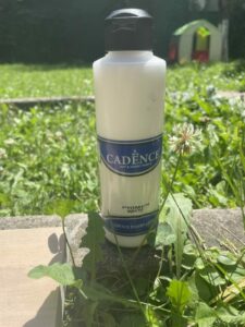 a bottle of gesso resting on the grass on a sunny day
