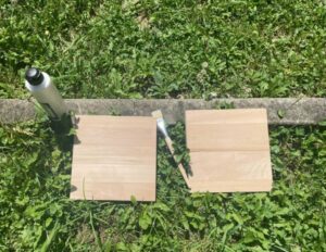 two square wooden panels on the grass with a paintbrush and a bottle of gesso next to them